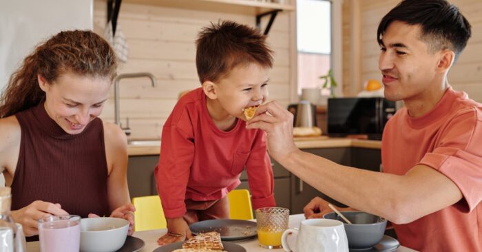 朝の食卓で親子が紅茶を飲みながら笑顔で会話する様子。カフェインレス紅茶を通じて穏やかな時間を共有するイメージ。