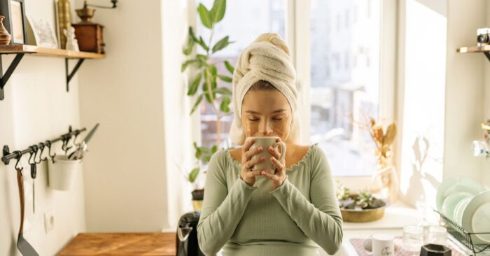 寝る前にカフェインレス紅茶を飲むママの様子。ベッドサイドで湯気の立つティーカップを持ち、穏やかな笑みを浮かべている。