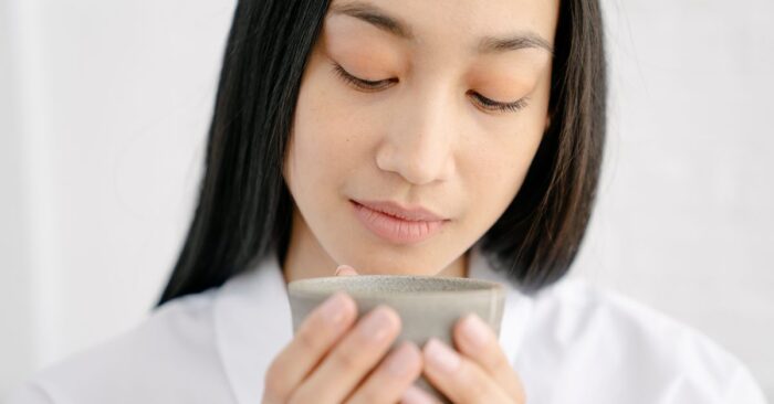 紅茶の香りを深く吸い込みながら微笑む女性。柔らかな午後の光が差し込むリビングの雰囲気。