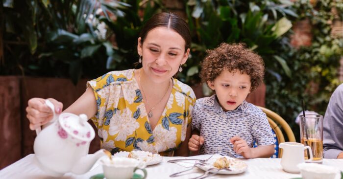 紅茶を手に優しく微笑むママ。窓辺のやわらかな光が差し込み、穏やかな幸福感に包まれている様子。